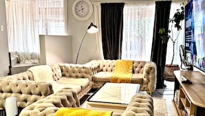 A living room with a sectional sofa, a coffee table, a clock, a lamp, and a television.