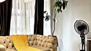 A living room with a tufted sofa, a yellow throw blanket, a potted plant, and a standing fan.