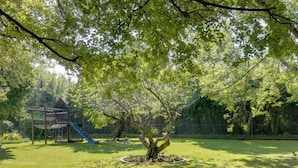 A well-maintained garden with a playground, including a slide and climbing structures, surrounded by a brick wall.