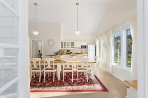 Une cuisine moderne avec des meubles blancs, un coin repas agrémenté d’un tapis à motifs rouges et de grandes fenêtres avec des rideaux.