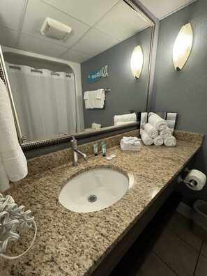 A bathroom with a granite countertop, a sink, a mirror, a towel rack, and a shower curtain. - Caravelle 1514 (Myrtle Beach)