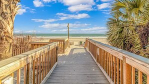 Ein hölzerner Steg führt zu einem Strand unter blauem Himmel.