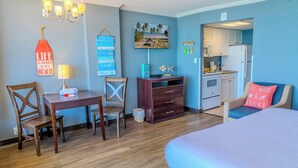 Ein Zimmer mit Bett, Schreibtisch, Stuhl, einer kleinen Küchenzeile und einem Fernseher.