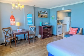 A room with a bed, a desk, a chair, a small kitchenette, and a TV.