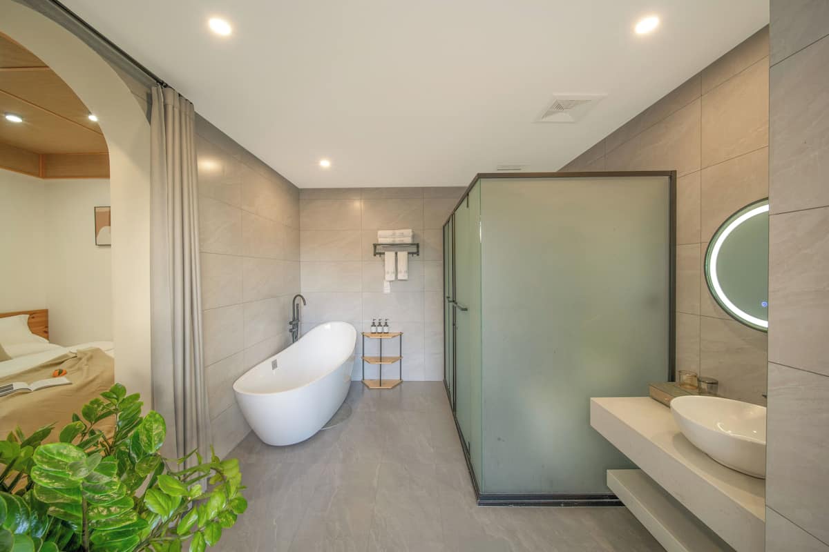 A modern bathroom with a freestanding bathtub, a glass-enclosed shower, and a vanity with a round mirror.