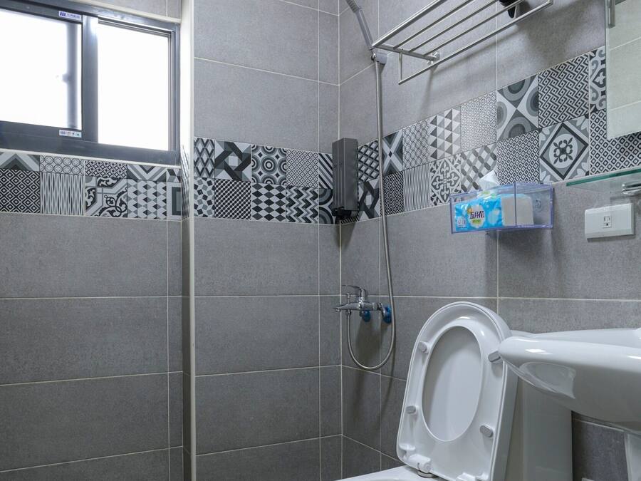 Casa de banho com sanita, chuveiro e um prateleira com artigos de higiene pessoal.