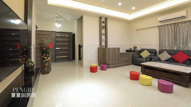 A modern living room with a sofa, coffee table, and colorful stools. There is a fireplace, a TV, and a decorative plant. - XIA XIA JIAO HOMESTAY (Magong)