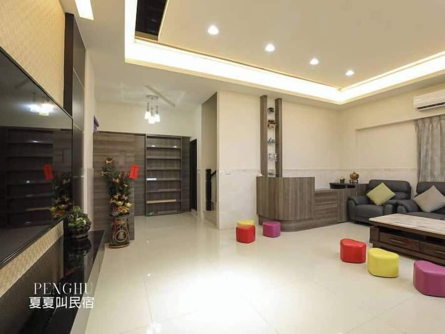 A modern living room with a sofa, coffee table, and colorful stools. There is a fireplace, a TV, and a decorative plant.