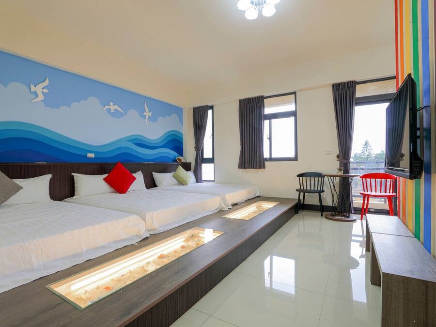 Quarto de hotel com duas camas, uma mesinha com cadeiras, uma televisão e um mural na parede.