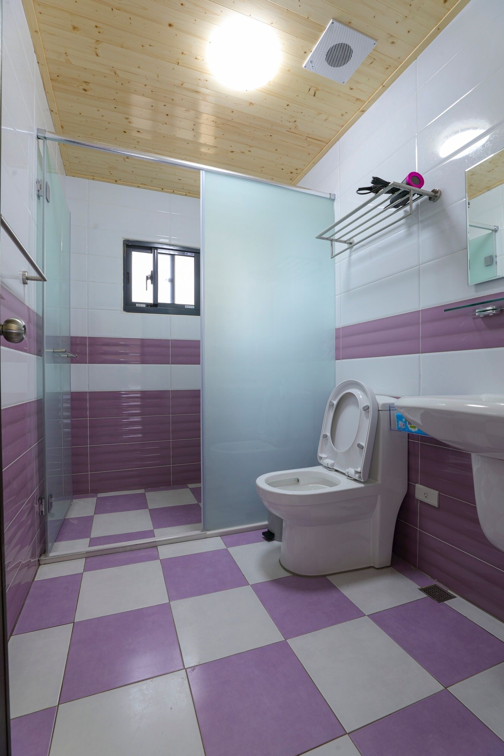 A bathroom with a checkered floor, a toilet, a shower with a glass door, and a sink with a mirror above it.