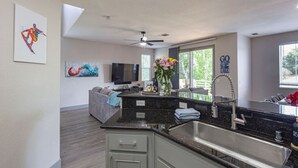 A modern kitchen with a large island, a built-in TV, and a dining area with a gray sofa. - Drifters Wake & Wine Getaway (Lake Tulloch)