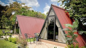 A modern A-frame structure with a patio area, outdoor seating, and lush greenery. - Tilawa La Fortuna Glamping (La Fortuna)