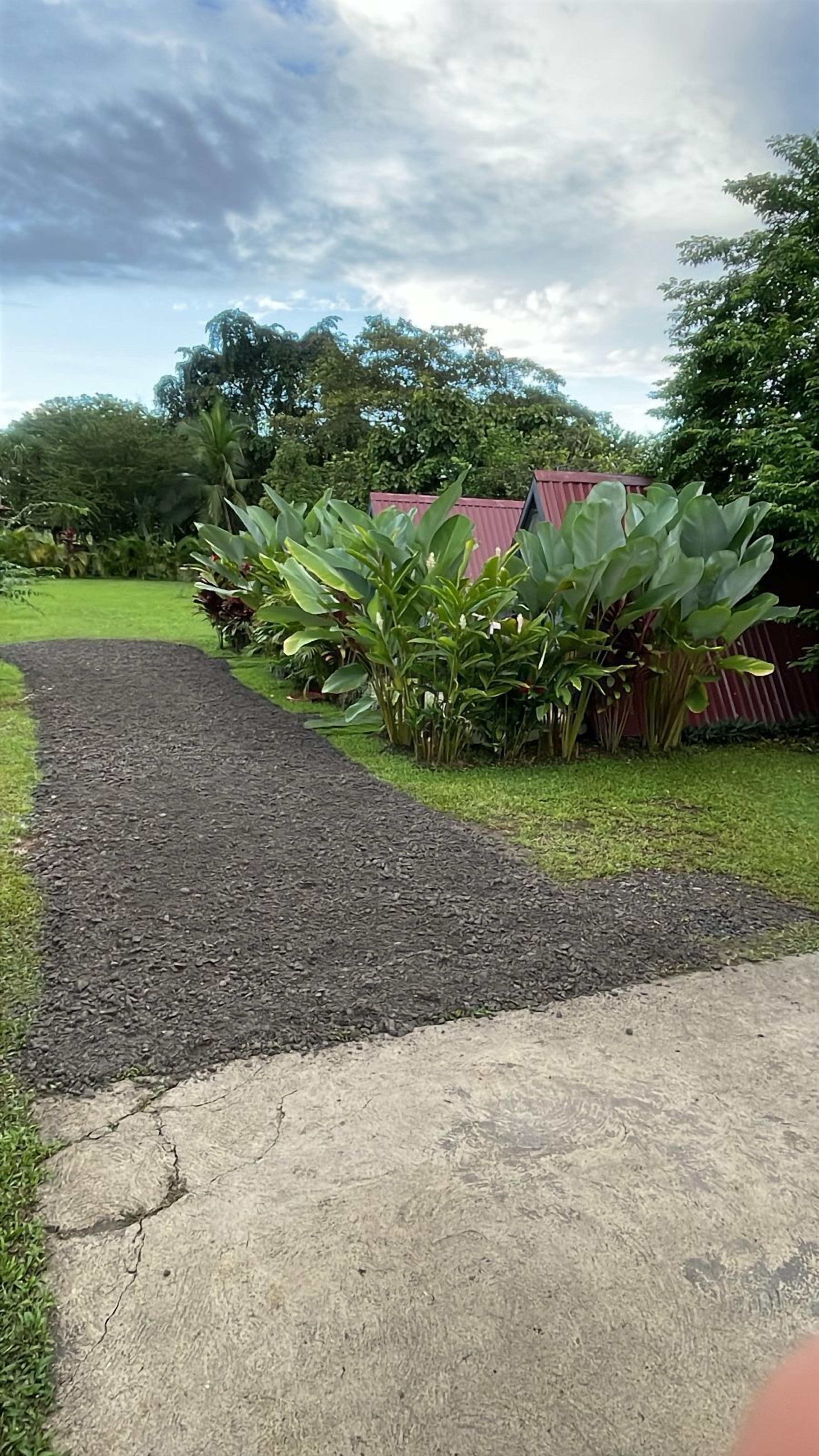 A pathway leading to a building with a red roof, surrounded by lush greenery and a clear sky.