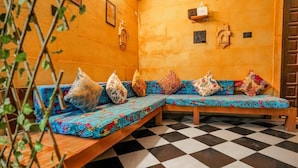 Una habitación de esquina con piso a cuadros, un banco de madera con cojines coloridos y un estante en la pared con un pequeño adorno.
