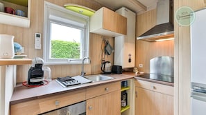 A compact kitchen with a window, a coffee maker, a kettle, and a stove. - Chalet 68 Village de la Mer (Saint-Hilaire-de-Riez)