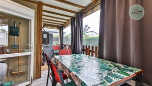 Een overdekt terras met een tafel en stoelen, een houten hek en een bordje met de tekst 'NOVA Convivialité'.