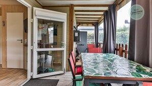 Een gezellige kamer met een schuifdeur naar een balkon, een eettafel met een tafelkleed met bladprint, en uitzicht op het omliggende landschap.