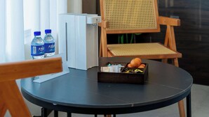 Une chambre d’hôtel moderne avec une table ronde, une chaise en bois, un petit meuble blanc et une grande plante verte.