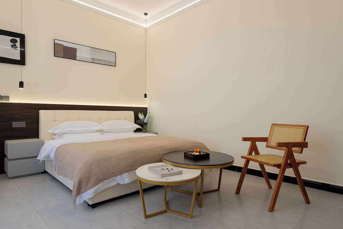 A neatly arranged bedroom with a bed, bedside tables, a small round table, and a wooden chair.