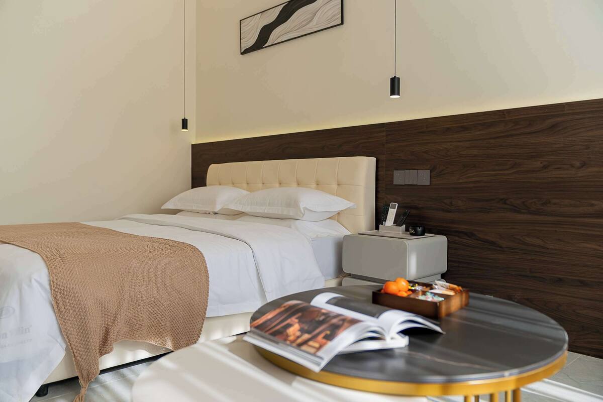 A hotel room with a bed, bedside table, and a round table with a magazine.