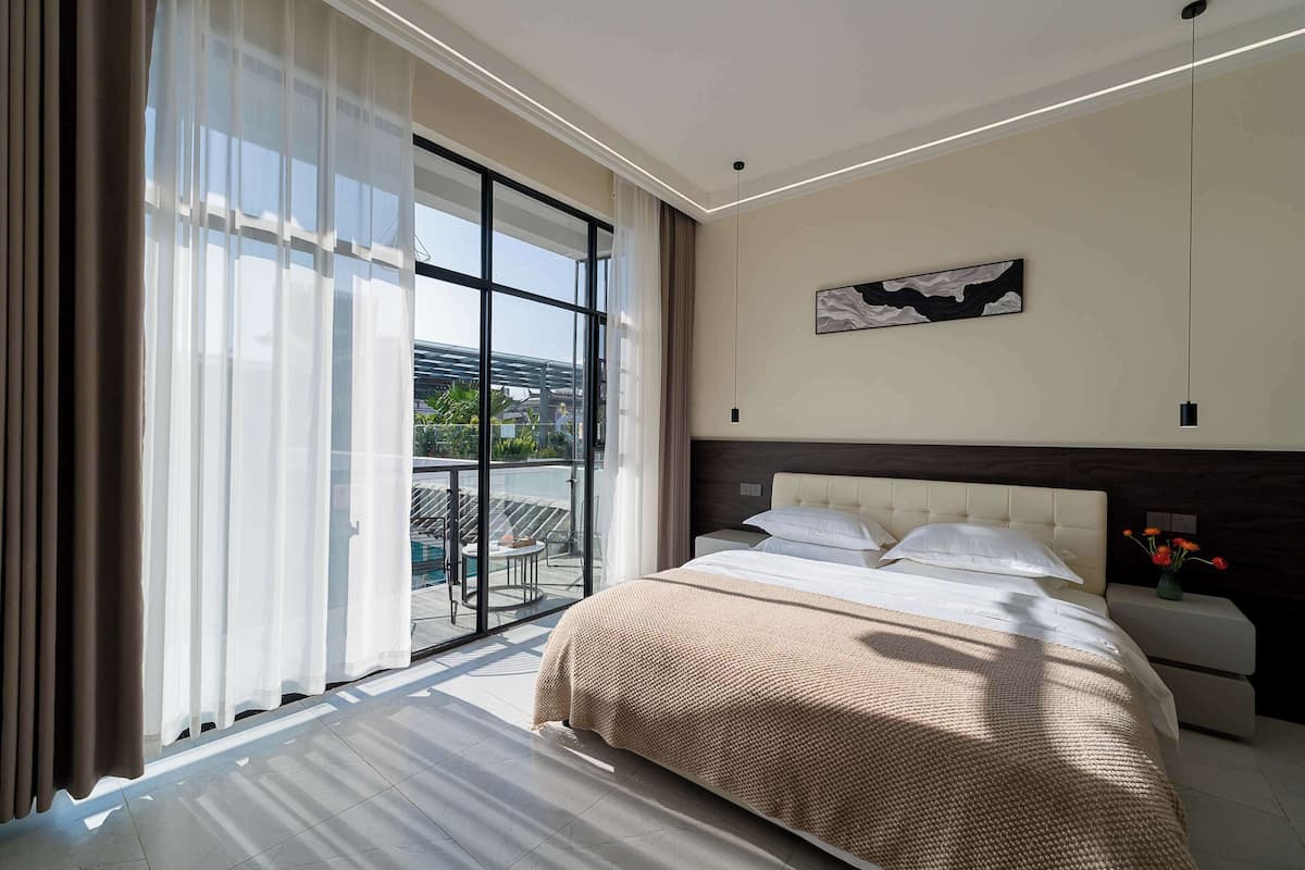 A modern hotel room with a large bed, a view through a glass door, and a minimalist decor.