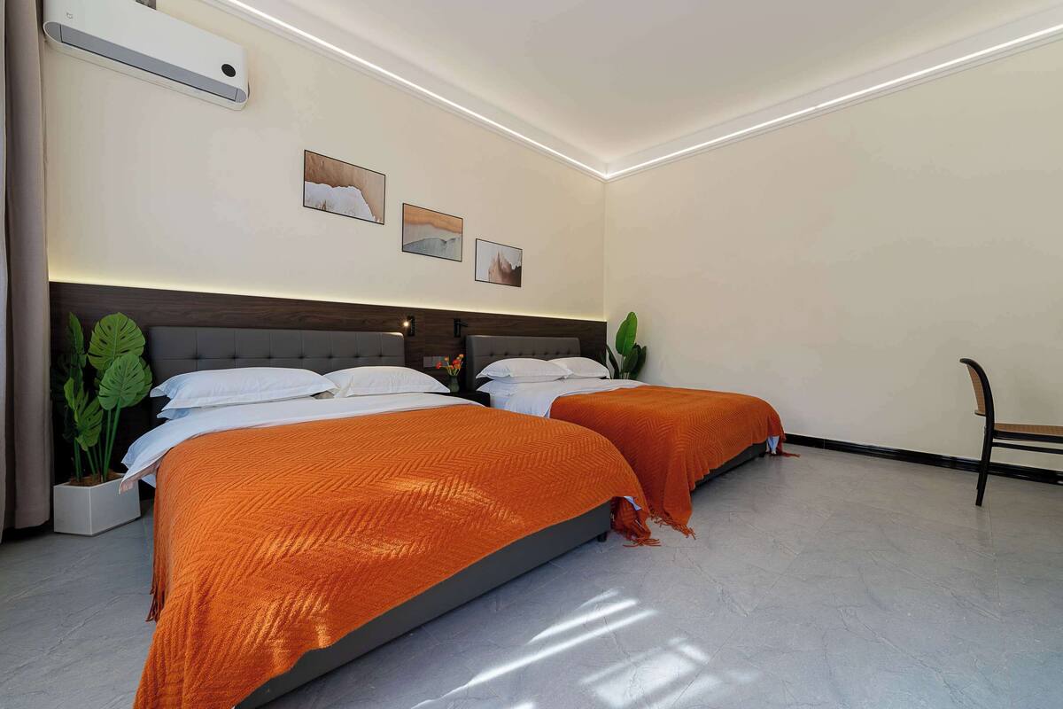 A hotel room with two beds, a large potted plant, and a modern design.