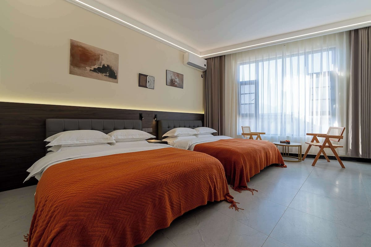 A hotel room with two beds, a small table, and a chair.