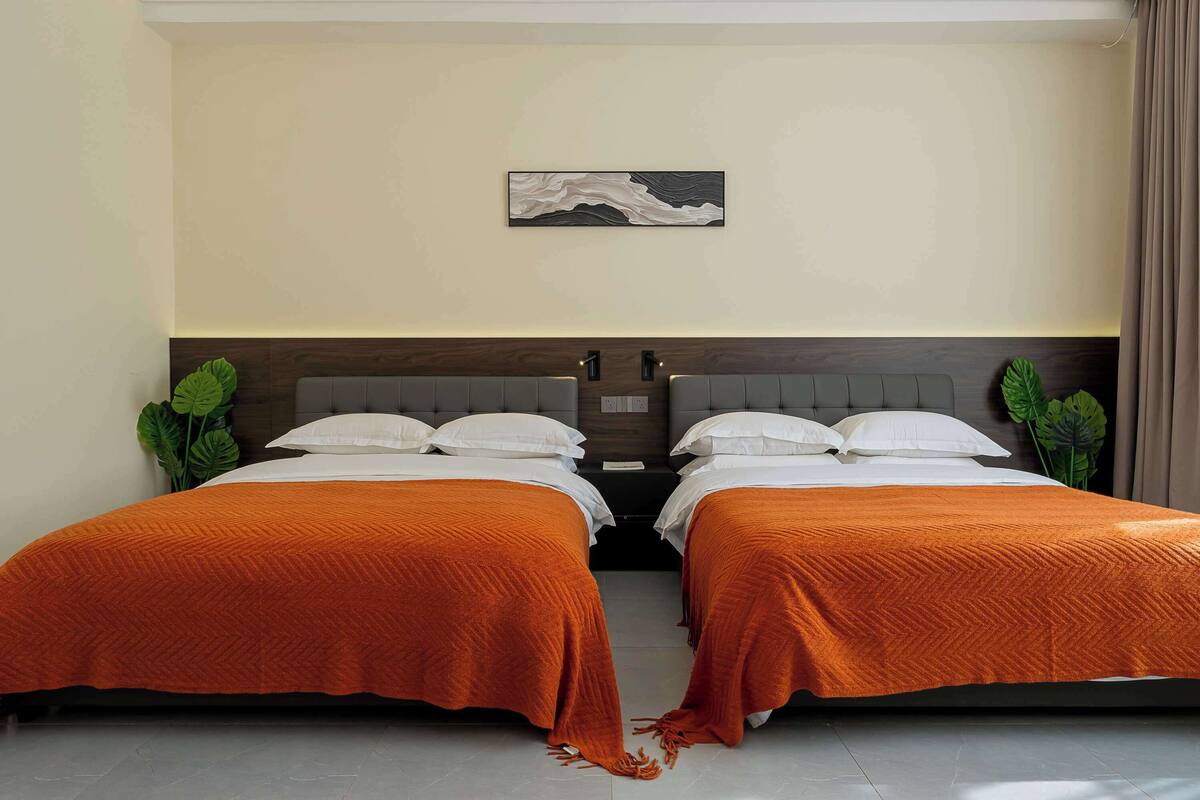 A double room with two beds, each with white bedding and orange throw blankets.