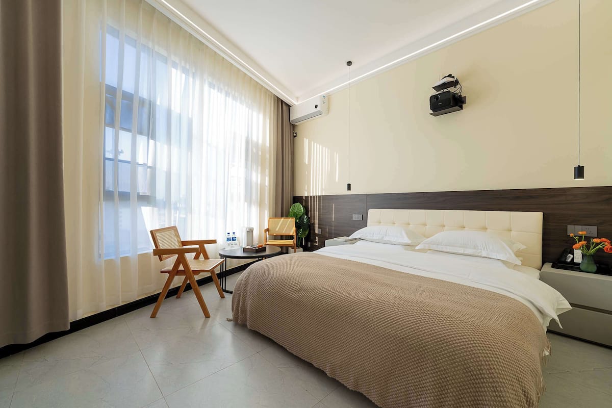 A hotel room with a large bed, a desk, a chair, and a window with curtains.
