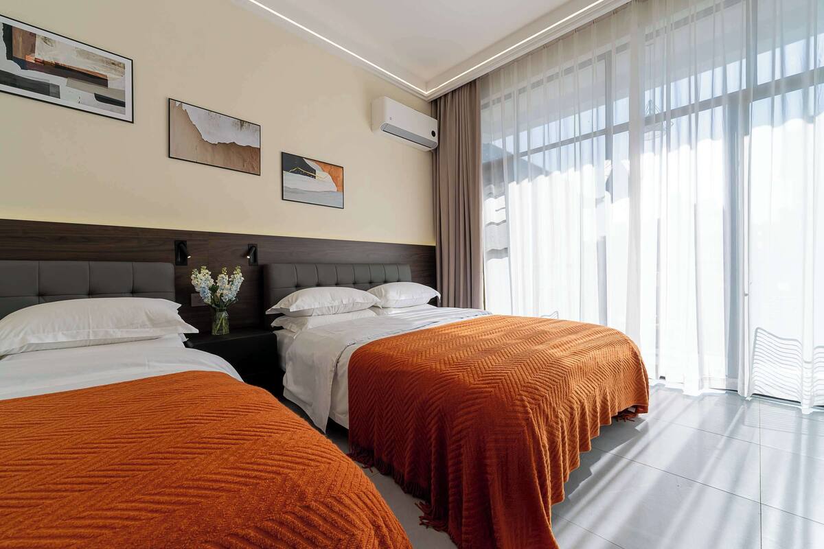 A hotel room with two beds, a large window with curtains, and artwork on the walls.