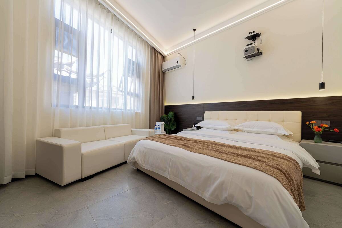 A modern bedroom with a large bed, a sofa, and a bedside table.