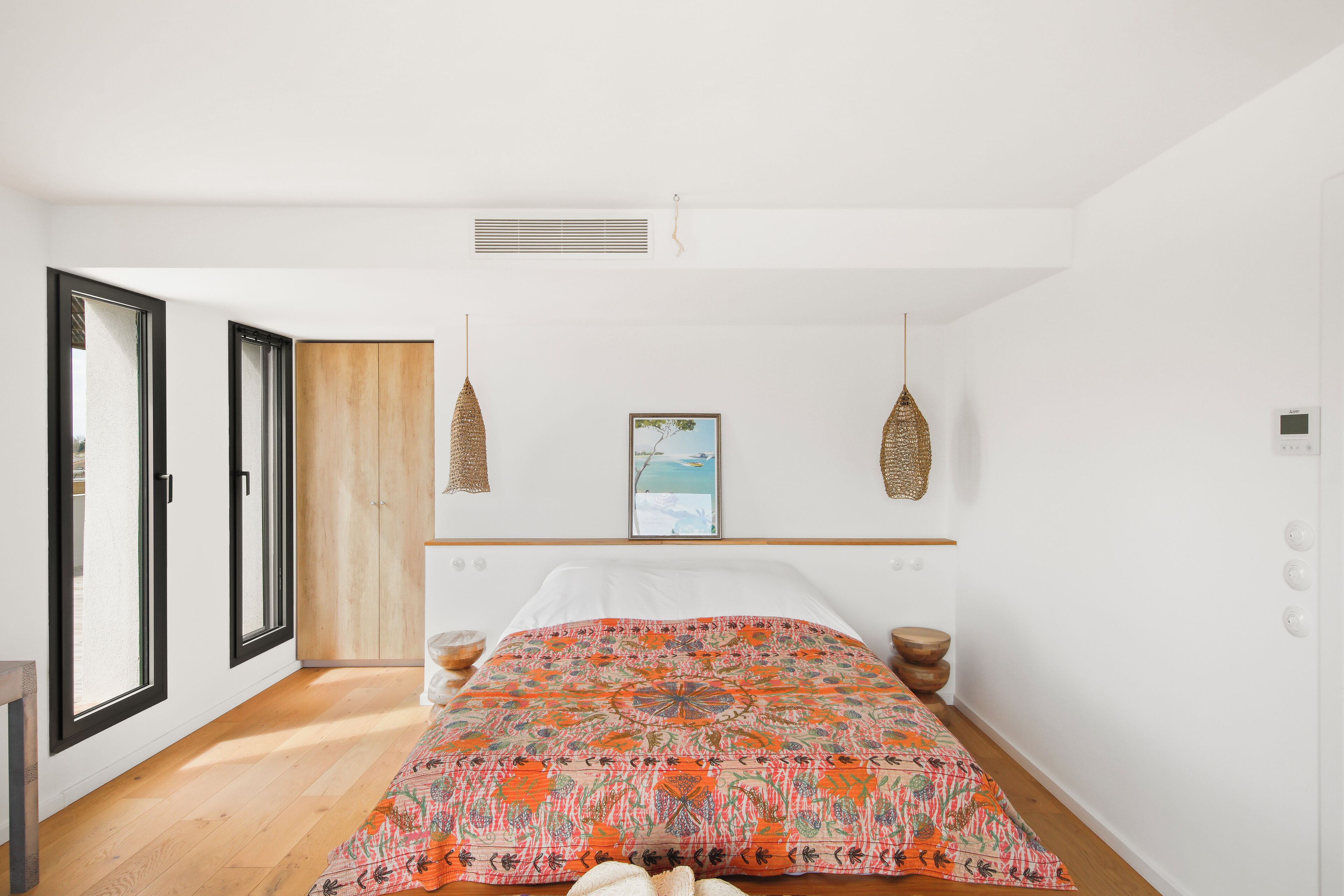 Un dormitorio con cama, un armario de madera, una ventana y una lámpara colgante.