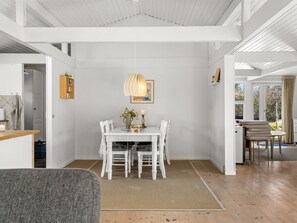Un coin repas avec une table et des chaises blanches, un luminaire suspendu et une vue sur l’extérieur.