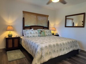A bedroom with a bed, two bedside lamps, a wooden headboard, a ceiling fan, a mirror, and a small rug.