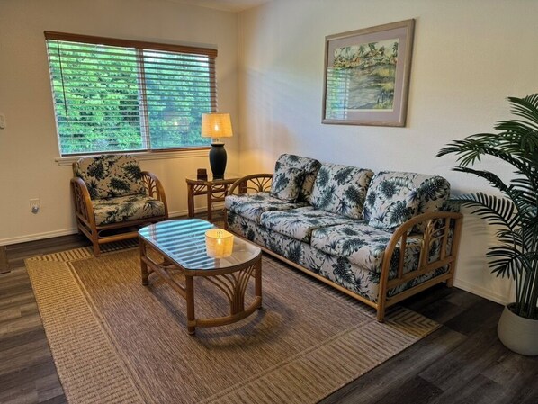 A living room with a sofa, two armchairs, a coffee table, a lamp, and a large window with blinds.