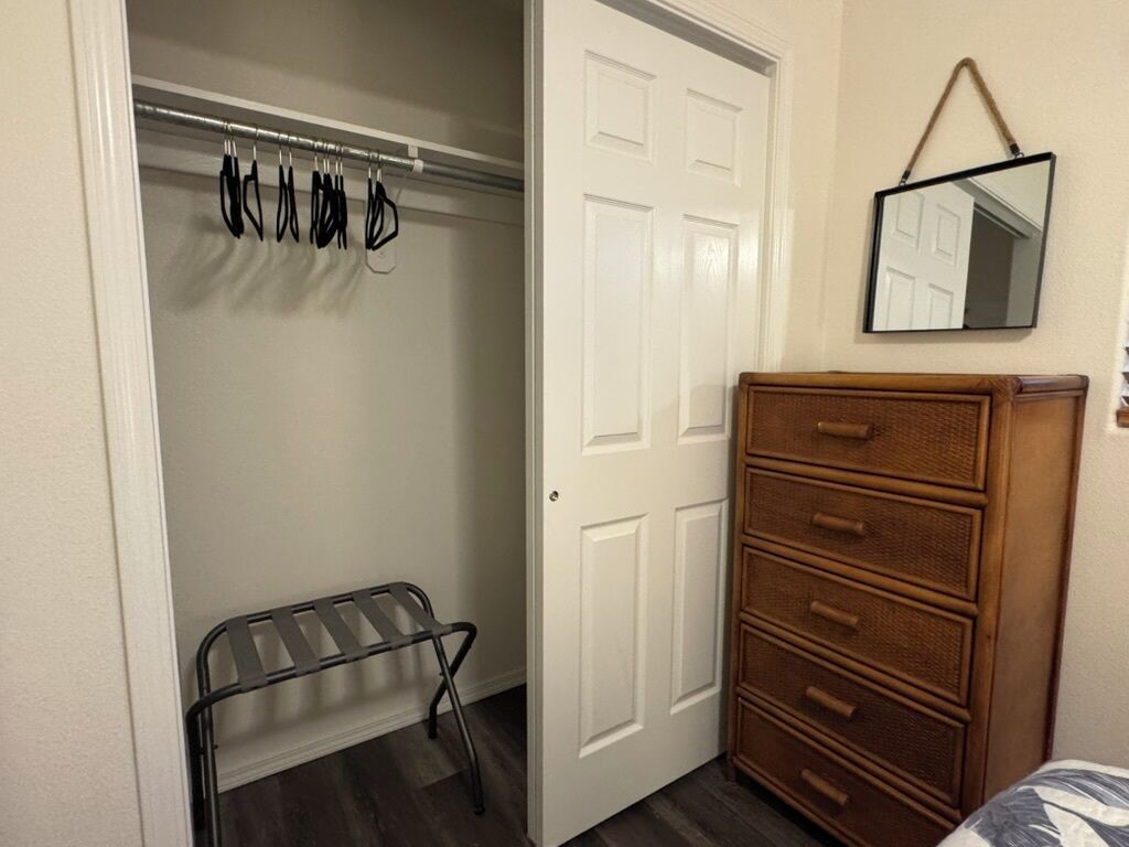A bedroom with a wooden dresser, a metal drying rack, and a white door.