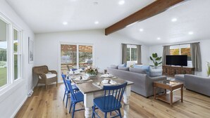 A modern living room with a dining area, grey sofas, a TV, and a wooden dining table.