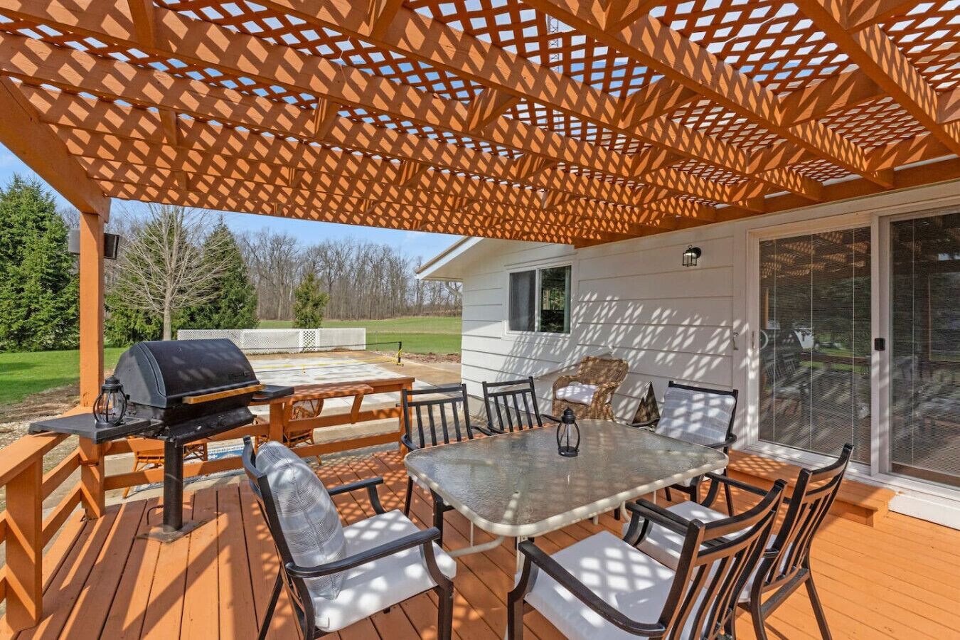 An outdoor patio with a wooden deck, a grill, and a table with chairs.