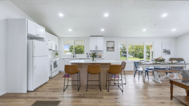 A modern kitchen with white cabinets, a central island with bar stools, and a dining area with a wooden table and chairs.