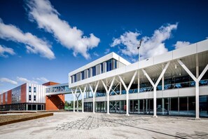 Situated on a spacious plaza, this building features a unique architectural design with large windows and a flat roof supported by white beams.