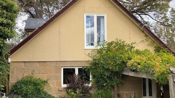 A two-story house with a stone facade, a gabled roof, and a small front porch. - Rose Cottage (Hamilton)