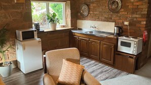 A compact kitchen with a refrigerator, microwave, and toaster. A chair with a cushion is placed in front of the sink. - Rose Cottage (Hamilton)