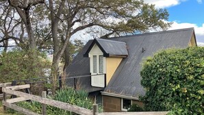 A house with a sloped roof, a wooden fence, and a garden area with various plants. - Rose Cottage (Hamilton)
