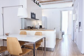Eine moderne Küche mit einer zentralen Kochinsel, weißen Schränken und Edelstahlgeräten. Es gibt einen Essbereich mit Tisch und Stühlen.