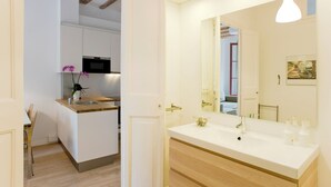 Una cucina moderna con mobili bianchi e un piano di lavoro in legno, un grande specchio sopra il lavello e un piccolo vaso con un'orchidea.