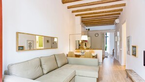 Un soggiorno con un divano angolare beige, una zona pranzo con tavolo e sedie, e una cucina sullo sfondo.