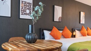 A hotel room with a wooden table, a vase with a plant, a bed with orange pillows, and artwork on the walls. - Seeds Nipponbashi (Osaka)