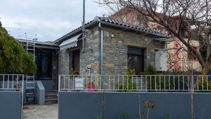 A stone house with a metal roof, a grey fence, and a mailbox labeled '77'. - Mona Lisa Guest House (Volos)