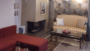 A living room with a red sofa, a glass coffee table, a fireplace, and a patterned wall. - Mona Lisa Guest House (Volos)