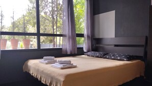 A modern bedroom with a large bed, a view of trees through the window, and a dark headboard. - Mona Lisa Guest House (Volos)